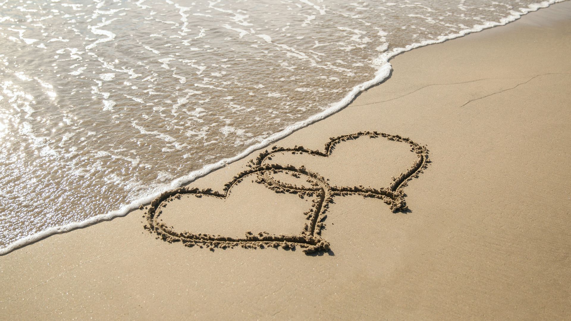 beach with two overlapping hearts drawn in the sand