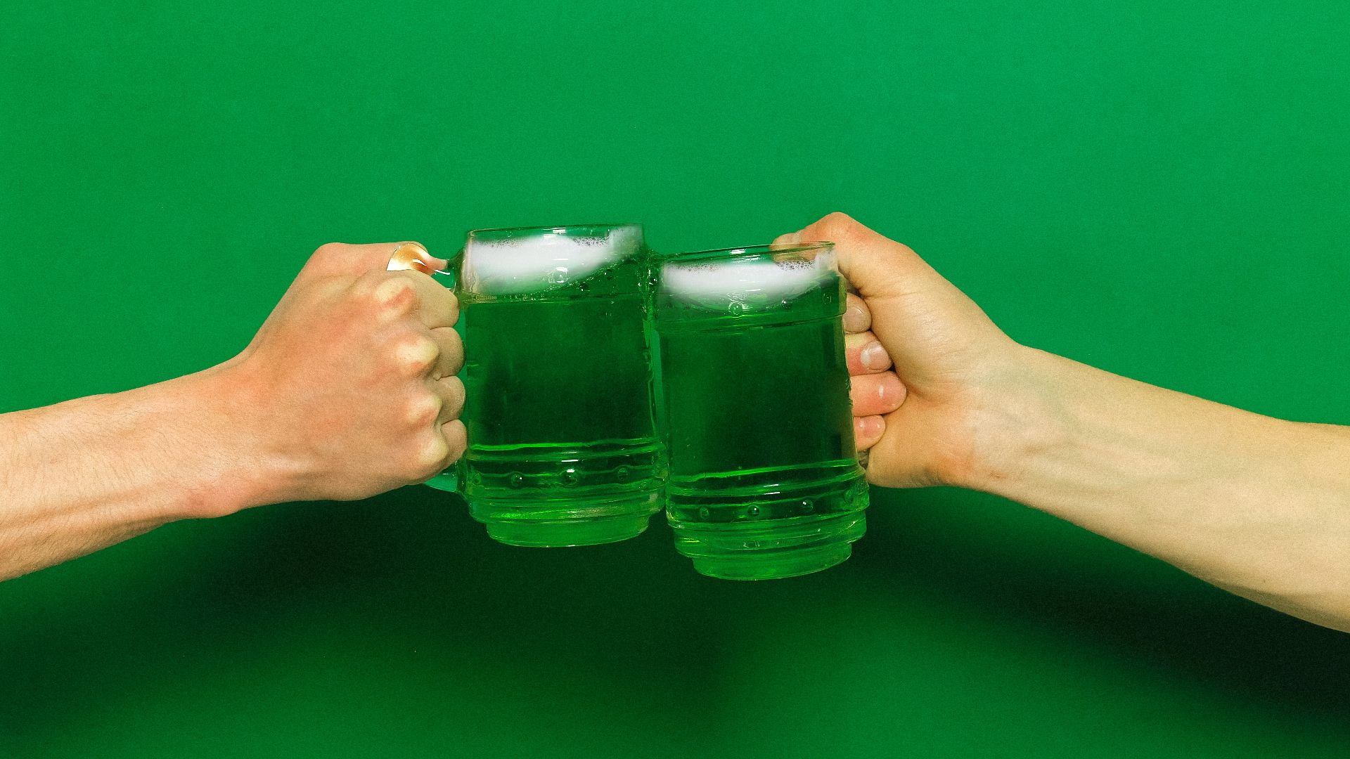 two people cheering mugs with green beer